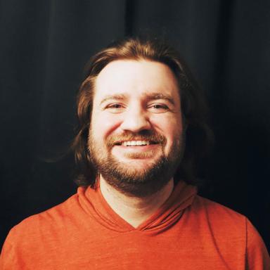 Matt Gehrls smiling in a headshot. He has long hair and short beard wearing a shirt that matches the color scheme of the website.